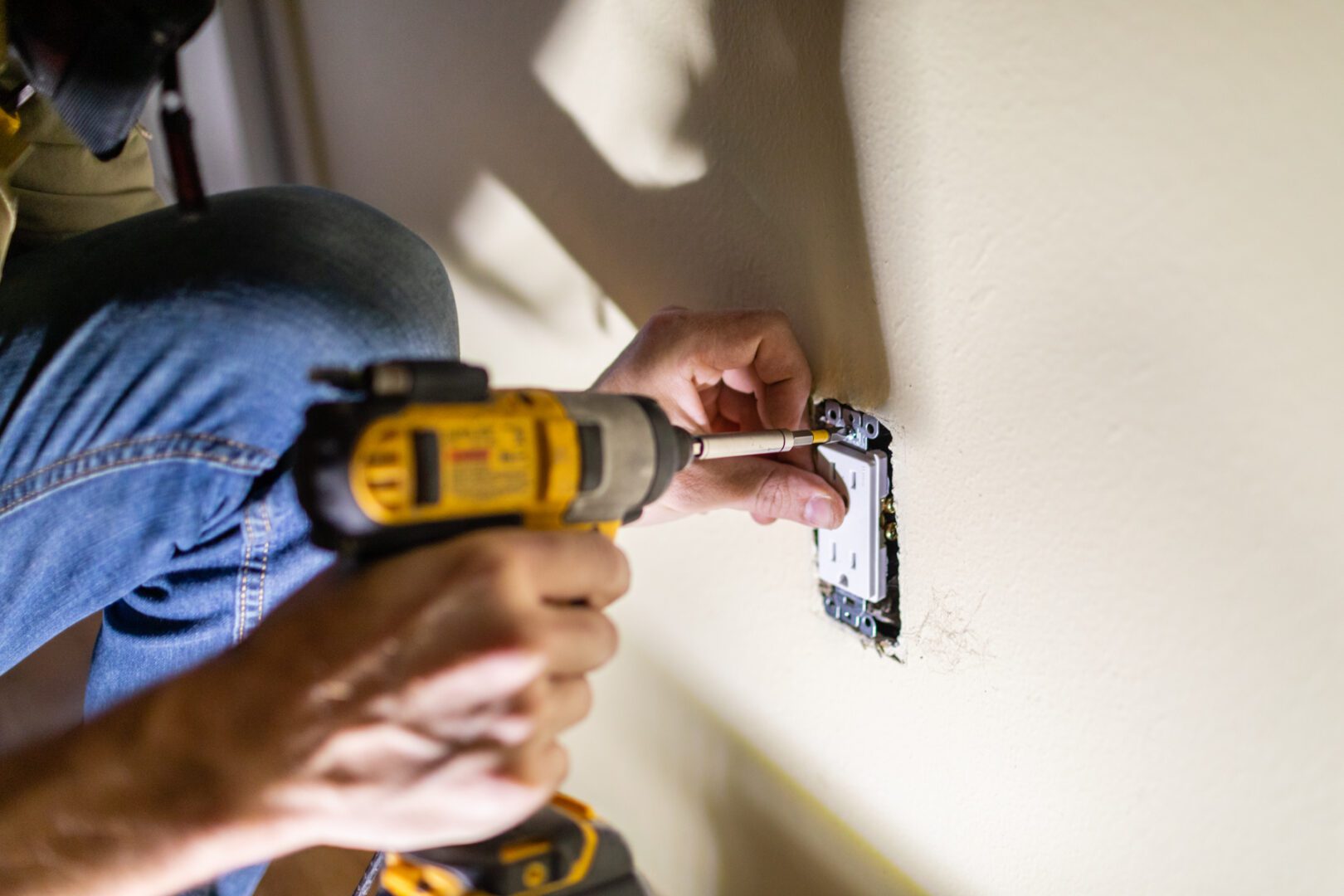 A person using a drill to install the electrical outlet.