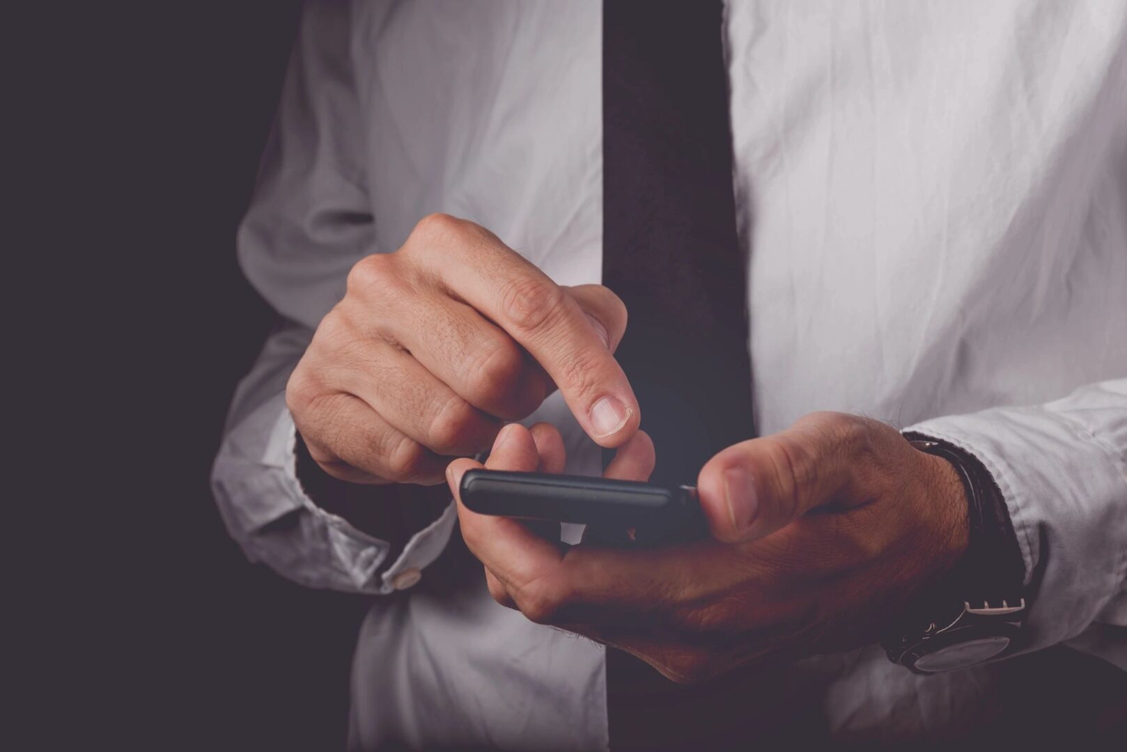 A man in a white shirt and tie holding a phone.